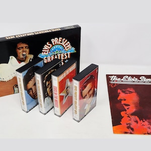 Puede incluir: Una colección de cintas de casete de música de Elvis Presley y un folleto titulado "The Elvis Story". Las cintas de casete presentan los mayores éxitos de Elvis Presley y Elvis en las películas. Las cintas de casete son negras con texto e imágenes rojas y blancas. El folleto es rojo con texto blanco y una imagen de Elvis Presley.