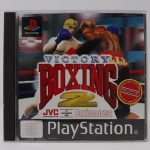 Peut inclure: Boîte de jeu PlayStation pour Victory Boxing 2, avec un ring de boxe rouge et blanc et deux boxeurs en arrière-plan. Le jeu est en association avec Boxing News et présente le logo Dual Shock.