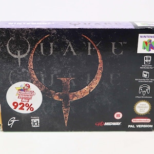 May include: A vintage Nintendo 64 video game box for "Quake." The box is primarily black with the game's title in a stylized, rusty orange font. A "Nintendo Essential Buy!" sticker is on the front, with a 92% rating. The box also features the Nintendo 64 logo.