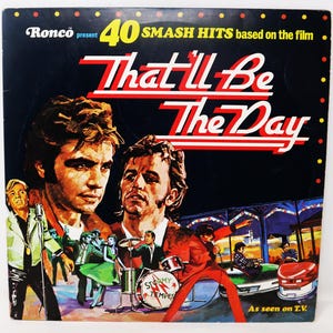 May include: A vinyl record album cover titled That'll Be The Day, featuring illustrations of two men in the foreground and a band performing on stage with bumper cars in the background. The text reads Ronco present 40 Smash Hits based on the film.