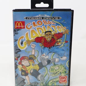 May include: A Mega Drive video game cartridge for Global Gladiators. The box art features cartoon illustrations of two young men, one in a red shirt and blue jeans, and the other in a soccer uniform. The McDonald's logo is visible.