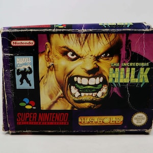 May include: A Super Nintendo game cartridge box for The Incredible Hulk. The box is purple and features a close-up image of the Hulk's face with a green mouth. The text "The Incredible Hulk" is printed in white on a black background. The box is labeled "U.S. Gold" and "Original Nintendo Seal of Quality".