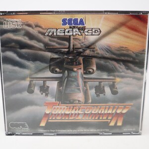 May include: A Sega Mega-CD game case with a red, white, and black design. The game is called Thunderhawk and features a helicopter flying through the clouds. The case is made of clear plastic and has a black background.