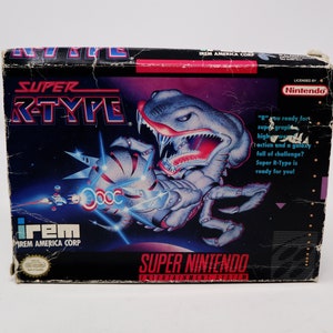 May include: Super Nintendo Entertainment System game cartridge box for Super R-Type. The box features a black background with a large image of a grey and blue alien creature with red eyes and a large mouth. The text "Super R-Type" is in white and red letters. The text "irem" is in white letters. The text "Licensed by Nintendo" is in white letters on a blue background.