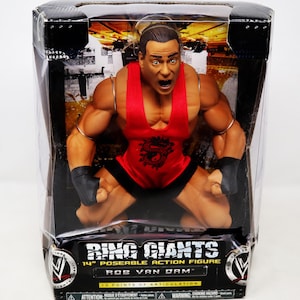 May include: A 14-inch action figure of Rob Van Dam in a red wrestling singlet with black wristbands. The figure is posed in a kneeling position with a determined expression on its face. The packaging features the Ring Giants logo and the text "13 Points of Articulation".