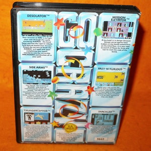 Puede incluir: Una caja azul y amarilla con una variedad de cartuchos de videojuegos. La caja presenta un diseño colorido con estrellas y la palabra "GO CRAZY" en letras grandes. Los cartuchos son para los juegos "Desolator", "Side Arms", "Thunderceptor", "Mission Elevator", "Fast N' Furious" y "Shackled".