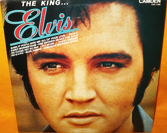 Può includere: Un primo piano del viso di Elvis Presley sulla copertina di un album in vinile nero. Il titolo dell'album "The King... Elvis" è stampato in lettere rosse e bianche. L'album è intitolato "The King... Elvis" e include i titoli delle canzoni "Baby, If You'll Give Me All of Your Love", "Relax", "Early Mornin' Rain", "One Broken Heart For Sale", "So Close, Yet So Far", "No More", "Happy Ending", "Ku-U-I-Po", "Blue Hawaii" e "Hawaiian Wedding Song". L'album è della casa discografica Camden e ha il numero di catalogo CDS 1190.