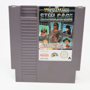 May include: A gray Nintendo Entertainment System game cartridge for Wrestlemania: Steel Cage Challenge. The front of the cartridge features a colorful image of four wrestlers in a steel cage. The text "Wrestlemania Steel Cage Challenge" is printed in white on a black background. The text "This Game Pak can only be used with the Mattel or NES versions of the Nintendo Entertainment System." is printed in black on a white background. The text "NES-WS-UKV" is printed in black on a white background. The Nintendo seal of quality is printed in the lower right corner.