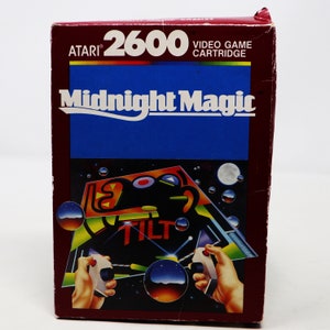 Puede incluir: Un cartucho de videojuego Atari 2600 vintage con una etiqueta roja, blanca y azul. La etiqueta dice "Midnight Magic" en letras blancas sobre un fondo azul. El cartucho de juego está en una caja de plástico con una etiqueta roja y blanca.