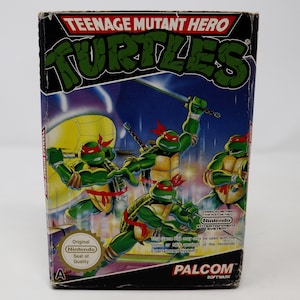 May include: Teenage Mutant Hero Turtles video game cartridge box art featuring four green turtles with red masks and weapons. The box is black with white text and a red banner. The text on the box reads "Teenage Mutant Hero Turtles" and "PALCOM SOFTWARE".