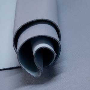 Puede incluir: Un rollo de tela de cuero azul claro. El cuero es suave y flexible, con una superficie ligeramente texturizada.