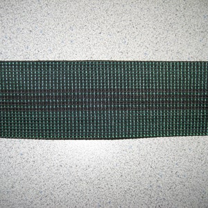 May include: A close-up of a green and black woven elastic band. The band has a grid pattern and is made of a durable material.