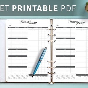 May include: An open ring-bound fitness planner with white pages featuring black text and grids for tracking meals, resistance training, and cardio. The text Fitness planner is printed at the top of each page. A blue ballpoint pen rests on the left page.