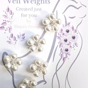 Può includere: Cinque pesi per velo a forma di fiore perlato con centri di strass sono esposti su sfondo bianco. Il testo "Veil Weights" e "Created just for you by Haya's Designs" è visibile. Sono presenti anche un'illustrazione floreale e la silhouette di una persona.