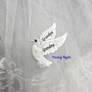 May include: A white dove embroidery patch on sheer white tulle fabric. The dove is depicted in flight facing right, with the word Grandpa embroidered on the upper wing and the word Grandma on the lower wing in dark thread.