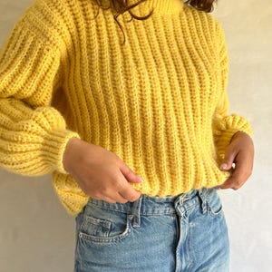 May include: A yellow ribbed knit sweater with long sleeves and a round neckline.