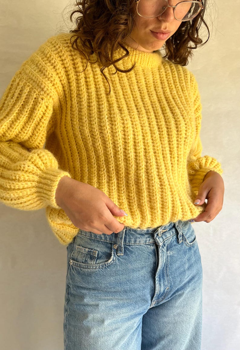 May include: A yellow ribbed knit sweater with long sleeves and a round neckline.