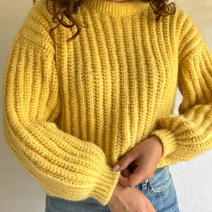 May include: A yellow ribbed knit sweater with long sleeves and a round neckline.
