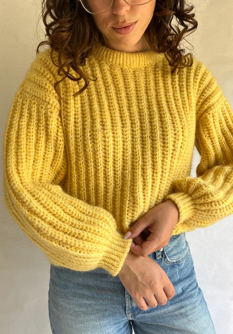 May include: A yellow ribbed knit sweater with long sleeves and a round neckline.