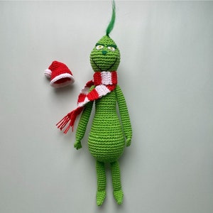 May include: Green crocheted Grinch doll with a red and white striped scarf and a red Santa hat.