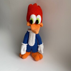 K&ouml;nnte beinhalten: Ein geh&auml;keltes Pl&uuml;schtier von Woody Woodpecker, einer Zeichentrickfigur. Das Spielzeug ist orange, blau und wei&szlig;. Es hat einen langen Schnabel und gro&szlig;e Augen.