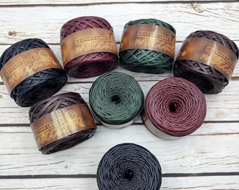 May include: Assortment of eight spools of macaron yarn in various colors, including black, brown, dark green, burgundy, and dark blue. Each spool has a label that reads "Leather Look Maccaron".