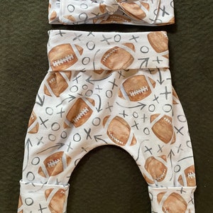 Pode incluir: Leggings brancos para beb&ecirc; com estampa de futebol marrom e branco. As leggings t&ecirc;m a parte inferior dobrada e uma faixa de cabe&ccedil;a combinando com um la&ccedil;o.