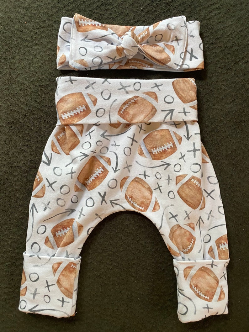 Pode incluir: Leggings brancos para beb&ecirc; com estampa de futebol marrom e branco. As leggings t&ecirc;m a parte inferior dobrada e uma faixa de cabe&ccedil;a combinando com um la&ccedil;o.