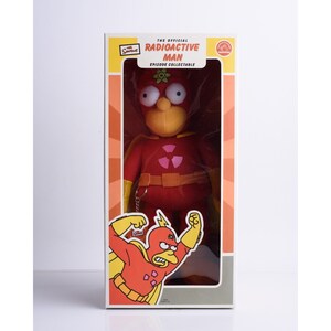 May include: The Official Radioactive Man Episode Collectible plush toy from The Simpsons. The plush toy is red with a yellow atomic symbol on the chest and a yellow face with large eyes. The toy is packaged in a box with a cartoon image of Radioactive Man.
