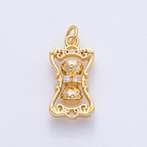 May include: A gold-colored hourglass pendant with a decorative frame. The hourglass shape features star and dot details, with two small clear stones at the center. The pendant has a loop at the top for a chain.