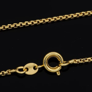 May include: A gold chain necklace with a lobster clasp closure. The chain is made of small, linked squares.