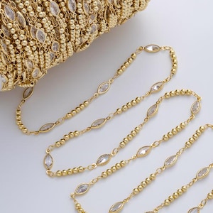 May include: A spool of gold-colored chain with alternating small beads and oval-shaped clear crystals. Several strands of the chain are unraveled, displaying the design. The chain is likely used for jewelry making or crafting.