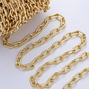 May include: A roll of gold-colored chain with a series of oval links. Several strands of the chain are unrolled and laid out on a white surface. The chain is likely used for jewelry making or crafting.