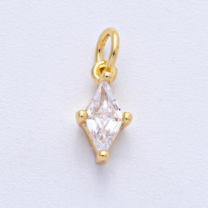 May include: A gold-colored charm with a clear, diamond-shaped cubic zirconia stone. The charm has a small loop at the top for hanging and is accented with small gold beads at the corners of the stone. The charm is on a white background.