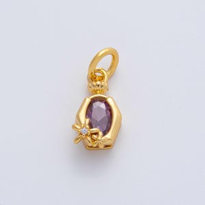 Pode incluir: Pingente dourado com uma pedra preciosa oval roxa no centro. O pingente tem uma moldura hexagonal e é adornado com pequenos detalhes florais, um dos quais apresenta uma pequena pedra transparente. Possui uma argola na parte superior para uma corrente.