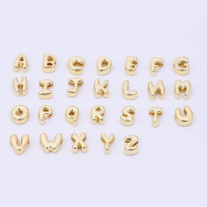 Könnte beinhalten: Eine Sammlung goldfarbener Buchstabenanhänger, jeweils mit einem abgerundeten, blasenartigen Design. Die Buchstaben A bis Z sind abgebildet, perfekt für personalisierten Schmuck oder Bastelprojekte. Das glänzende, metallische Finish verleiht einen Hauch von Eleganz.