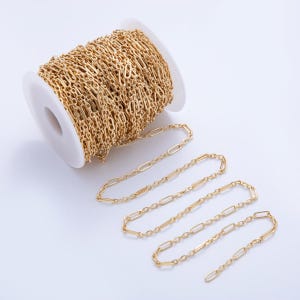 May include: A spool of gold-coloured chain featuring an elongated oval and bar link design. Several strands of the chain are unraveled, showcasing the pattern. The chain is likely used for jewellery making or other craft projects.