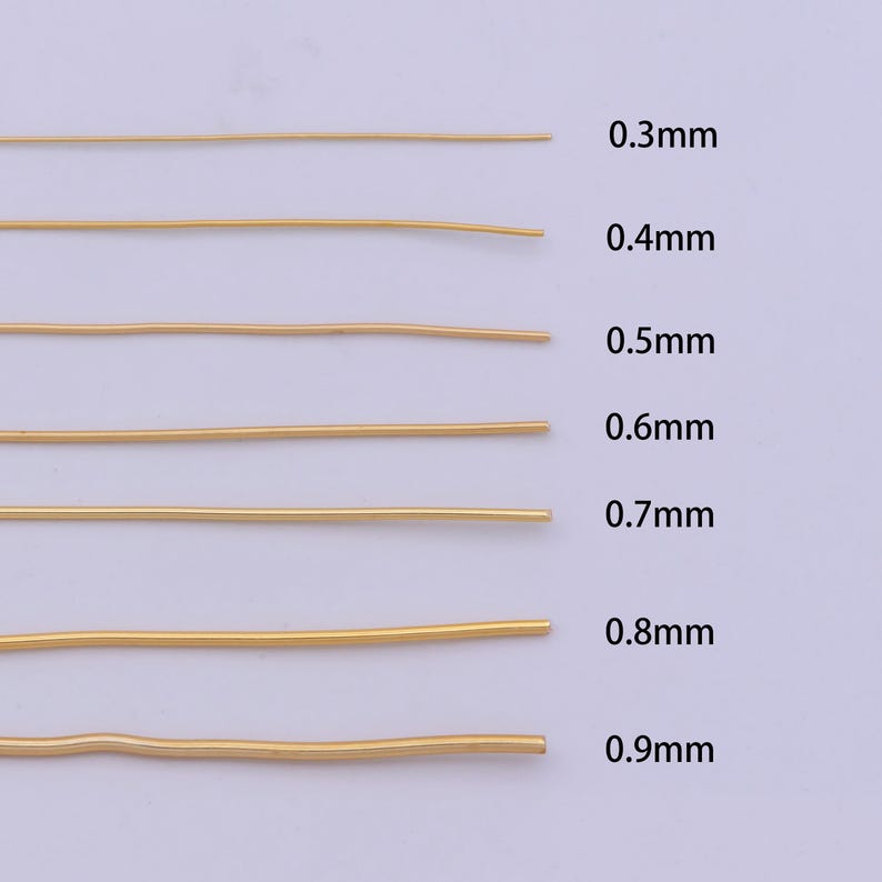 Pu&ograve; includere: Sette pezzi di filo d'oro, ognuno di uno spessore diverso, disposti orizzontalmente su una superficie bianca. Gli spessori del filo sono etichettati come 0,3 mm, 0,4 mm, 0,5 mm, 0,6 mm, 0,7 mm, 0,8 mm e 0,9 mm.
