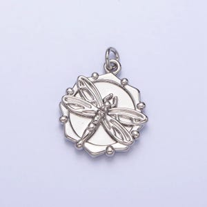 May include: Silver pendant featuring a detailed dragonfly design inside a circular frame with a textured edge.