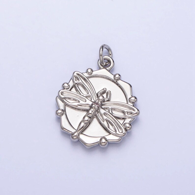 May include: Silver pendant featuring a detailed dragonfly design inside a circular frame with a textured edge.