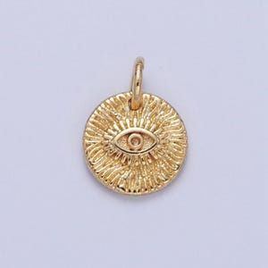 Könnte beinhalten: Goldfarbener Anhänger mit einem detaillierten bösen Auge mit einem blauen Zentrum. Der Anhänger ist rund und hat eine strukturierte Oberfläche.