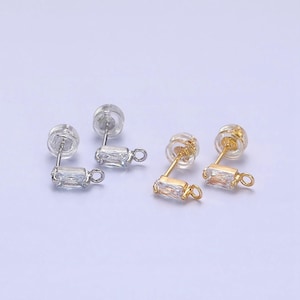 May include: Two pairs of earring findings with a clear rectangular stone and a silver or gold jump ring. The findings are made of metal and have a clear plastic post.