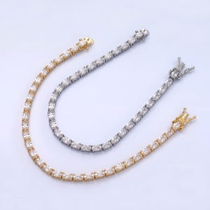 May include: Two tennis chain bracelets, one gold and one silver, with oval-shaped cubic zirconia stones.