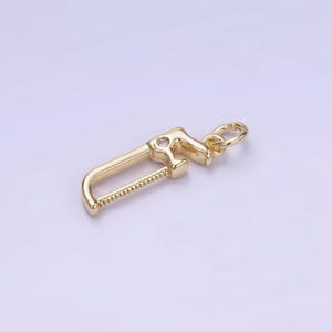May include: Gold-toned saw charm with a small clear rhinestone. The charm has a loop for attaching to a bracelet or necklace.