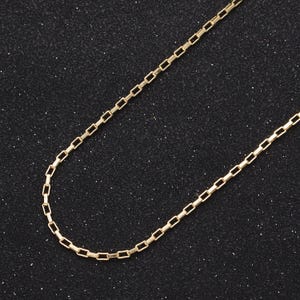 May include: A gold chain necklace with a box chain design. The chain is on a black background.