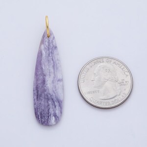 May include: A teardrop-shaped pendant with a gold-colored bail. The pendant is a marbled lavender and white stone. A U.S. quarter is next to the pendant for size comparison. The pendant is likely for jewelry.