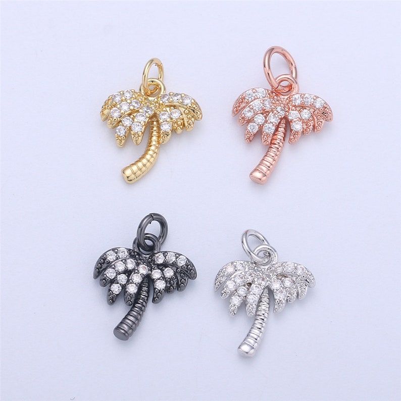 May include: Four palm tree charms with clear crystal accents. The charms are in gold, rose gold, silver, and black.