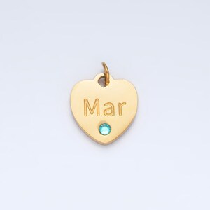 May include: Gold heart-shaped pendant with the name "Mar" engraved on it and a light blue gemstone in the center.