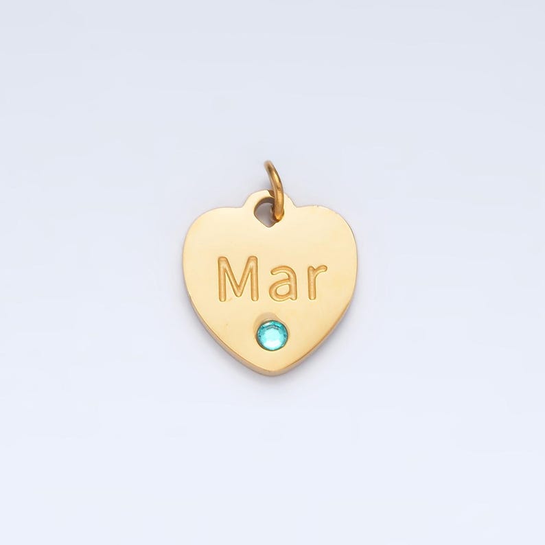 May include: Gold heart-shaped pendant with the name "Mar" engraved on it and a light blue gemstone in the center.