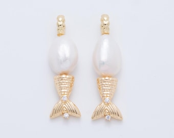 May include: A pair of gold-colored earrings with a mermaid tail design. Each earring features a large, white, teardrop-shaped pearl, a textured gold-colored midsection, and a gold-colored mermaid tail with a small, clear gem. The earrings are set against a white background.